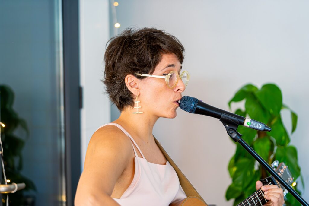 A woman sings into a microphone while playing guitar indoors, expressing musical passion.