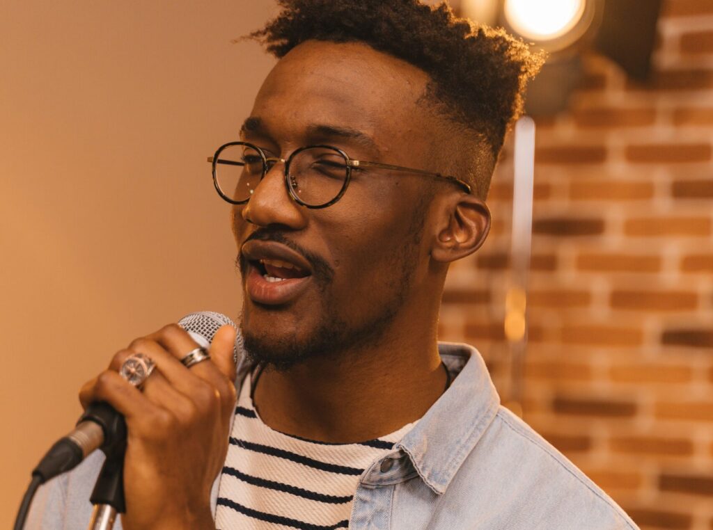 Portrait of a stylish black musician passionately singing with a microphone indoors, wearing a denim jacket.